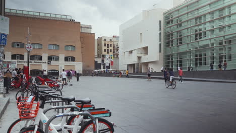Barcelona---Plaça-dels-Àngels,-outside-the-Musuem-of-Contemporary-Art-with-tourists,-skateboarders-and-bikes