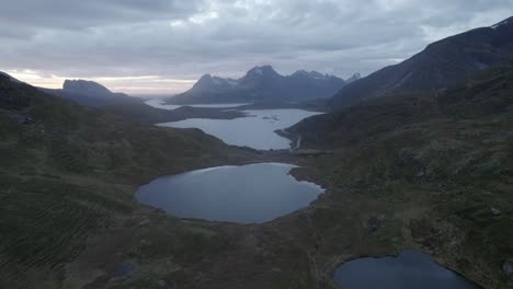 Aerial-view-over-ponds-and-raw-nature-with-mountainous-fjord-background,-in-gloomy-Lofoten,-Norway