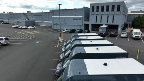 Amazon-delivery-vans-and-trucks,-aerial-rising-to-Amazon-Hub-warehouse-sign-and-smile-logo