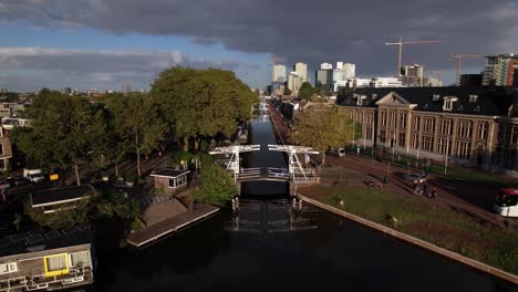 Descending-aerial-showing-Muntgebouw-museum-in-Utrecht-closing-in-on-small-white-draw-bridge-over-the-canal-on-a-bright-sunny-day-with-cloud-formation-in-the-background