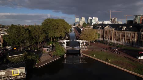 Antena-Descendente-Que-Muestra-El-Museo-Muntgebouw-En-Utrecht-Acercándose-A-Un-Pequeño-Puente-Blanco-Sobre-El-Canal-En-Un-Día-Soleado-Con-Formación-De-Nubes-En-El-Fondo