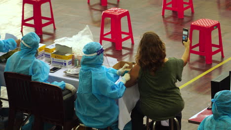 Mujer-Recibiendo-La-Vacuna-Covid-En-El-Centro-De-La-Clínica,-Tomándose-Selfie,-A-Pie-Felizmente