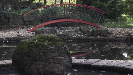 Pan-shot-of-a-pond-and-the-surroundings-covered-in-autumn-leaves,-a-moss-stone-and-arched-bridge-add-to-the-Oriental-setting-of-the-beautiful-wedding-and-banquet-venue,-Excellency-Midlands,-England