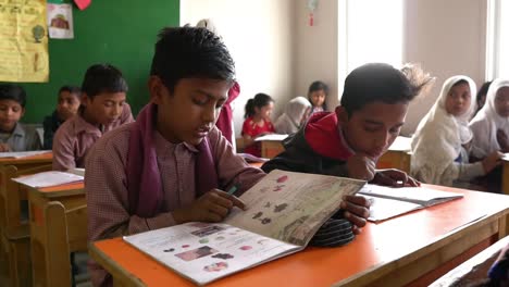 Dos-Jóvenes-Escolares-Musulmanes-Leyendo-Un-Libro-En-El-Escritorio-En-El-Aula-En-Karachi,-Pakistán