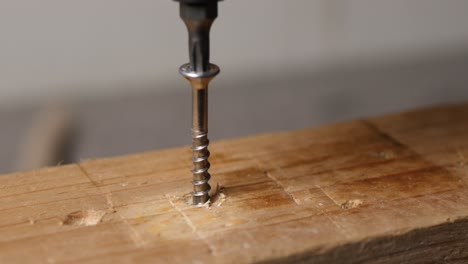 Close-up-unscrewing-a-bolt-out-of-a-wooden-plank-with-a-cordless-screwdriver
