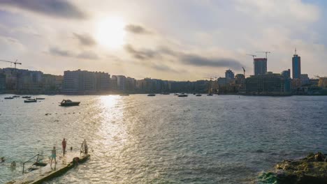 Timelapse-of-people-swimming-with-boats-at-anchor-in-Sliema,-Malta,-Mediterranean