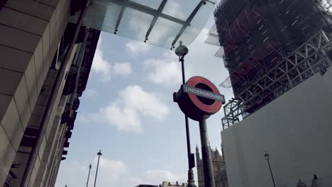 Aufnahme-Eines-Londoner-U-Bahn-Schildes-Am-Bahnhof-Westminster,-Auf-Der-Anderen-Straßenseite-Eine-Geschlossene-Baustelle,-Während-Der-Berühmte-Big-Ben-Einem-Restaurierungsprojekt-Unterzogen-Wird,-Westminster,-London,-England