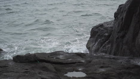Grey-moody-day-while-ocean-waves-hitting-rocky-coastline,-static-view