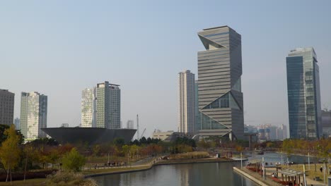 G-Tower-and-IBS-Tower-office-Skyscrapers-and-Tri-bowl-Exhibition-building-Skyline-in-Incheon-Songdo-Central-Park-in-Autumn-with-People-Relaxing-by-the-Lake---aerial-static