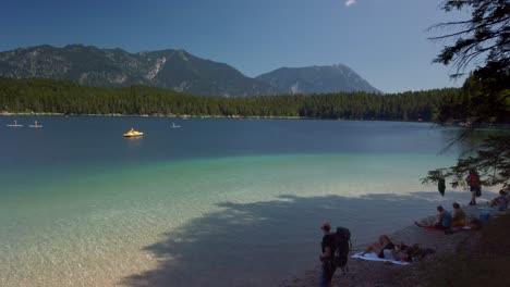 Beach-of-the-beautiful-Eibsee-lake-in-Bavaria,-very-close-to-the-Zugspitze-mountain,-with-people-and-pedal-boats
