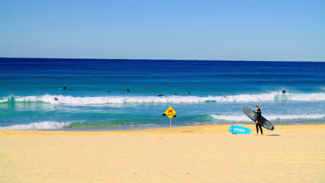 Surfers-Surfing-At-Bondi-Beach-With-Warning-Sign-In-Sydney,-New-South-Wales,-Australia