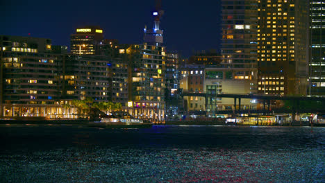 Ferry-Boat-Cruising-At-Port-Jackson-With-Illuminated-Skyline-At-Night-In-Sydney,-NSW,-Australia