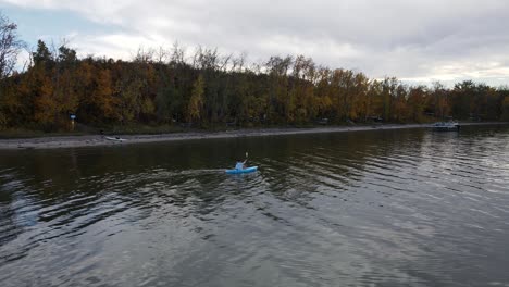 Woman-in-a-blue-kayak-paddling-along-the-colourful-shoreline-of-buffalo-lake-in-autumn