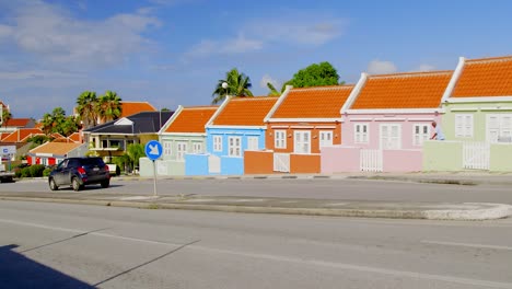 Row-of-colorful-and-picturesque-houses-on-Berg-Altena-Road-with-cars-driving-by-in-Willemstad-on-the-Caribbean-island-of-Curacao