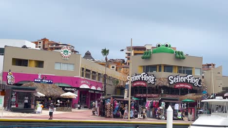 Senior-Frogs-and-other-building-fronts-in-the-marina-with-boat-in-Cabo,-Mexico