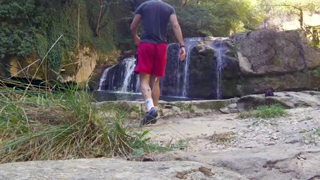 Slow-motion-of-a-boy-going-to-a-waterfall-and-lake-in-the-woods