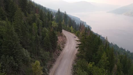 Silver-van-driving-along-a-dusty-forest-service-road-in-Canada-during-wildfire-season-with-Adams-Lake-in-the-background