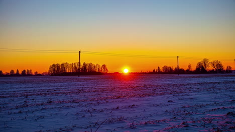 Ein-Zeitraffervideo-Eines-Sonnenuntergangs-über-Dem-Ackerland,-Aufgenommen-Im-Winter,-Wenn-Schnee-Den-Boden-Bedeckt