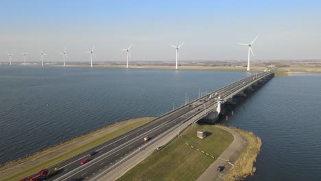 Aerial-orbit-over-bascule-bridge-with-traffic,-wind-turbines-in-distance,-Netherlands