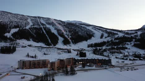 Skigebiet-Hemsedal-Nach-Sonnenuntergang-Und-Geschäftsschluss-–-Schöne-Luftaufnahme,-Die-Teilweise-Beleuchtete-Skipisten-Im-Hintergrund-Mit-Hotel--Und-Apartmentgebäuden-Davor-Zeigt-–-Luftaufnahme