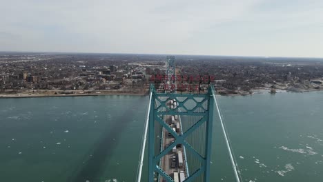 Ambassador-bridge-sign-and-endless-line-of-semi-trucks-piling-on-it,-aerial-view
