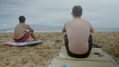 Close-up-shot-of-two-shirtless-man-sitting-on-the-near-the-sea-enjoying-beautiful-weather