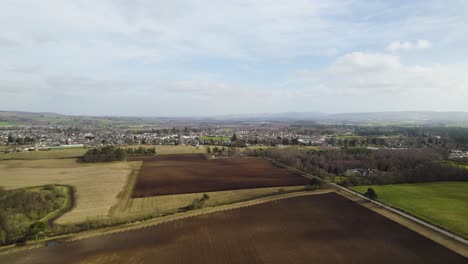 Drone-Aéreo-Volando-Hacia-El-Tractor-Arando-Un-Campo-En-La-Zona-Rural-De-Perthshire,-Escocia