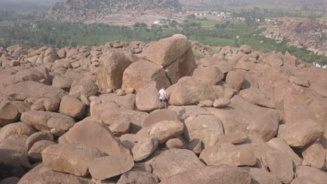 Aerial-follows-lone-male-tourist-in-mountain-of-granite-rock-boulders