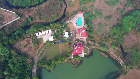 Summer-House-Aerial-Drone-view-with-Lake,-Trees,-Red-Roofs,-and-Swimming-Pool-in-Vadodara,-India