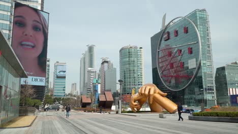 Koreans-in-Face-Masks-Walk-next-to-Starfield-Coex-Mall-in-Gangnam,-Seoul-with-a-beautiful-city-centre-skyline-and-many-skyscrapers-in-business-district