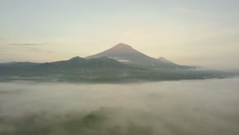 Mystic-Aerial-forward-flight-over-tropical-landscape-covered-with-fog-during-sunny-and-cloudy-day---Massive-Mount-Sumbing-in-background