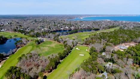 Osterville-township-near-green-and-vibrant-golf-course-field,-aerial-view