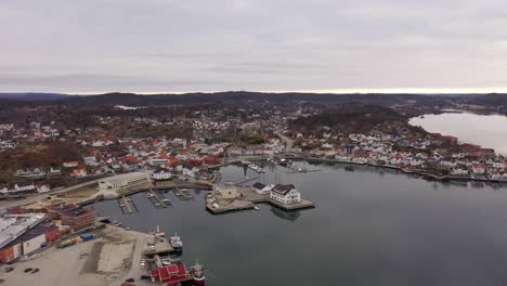 Beautiful-Grimstad-city-and-coastal-Marina-during-early-morning-with-reflections-in-sea---High-altitude-aerial-overview-descending-and-approaching-idyllic-marina-bay-close-to-sea-surface---Norway