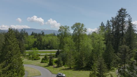 Cars-parked-at-a-rest-stop-in-Bellingham,-Washington-with-a-boom-up-to-reveal-the-highway-and-landscape-with-mountains-and-beautiful-blue-sky