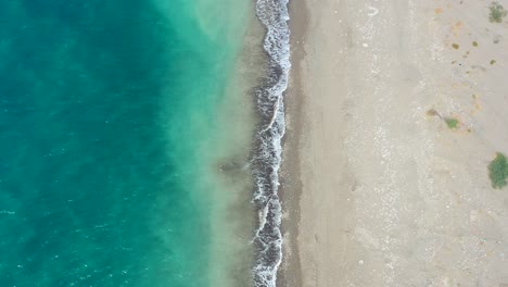 aerial-top-down-view-with-one-half-blue-tropical-ocean-and-the-other-half-an-empty-sandy-beach-with-waves-crashing-on-a-sunny-summer-day