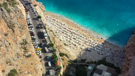 Aerial-drone-circling-Kaputas-Beach-during-sunset-in-Kas-Turkey-as-cars-drive-looking-for-parking-and-tourists-lay-out-on-the-white-sand-beach-and-blue-turquoise-water-during-summer