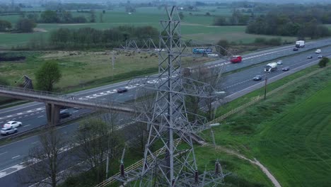 Speeding-traffic-passing-pylon-electricity-tower-on-M62-motorway-aerial-view-close-up-descending-orbit-left