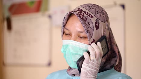 Smiling-Indonesian-female-nurse-close-up-talking,-using-smartphone,-friendly-professional-nurse-therapist-or-patient-consulting-a-midwife,-discussing-medical-examination-results-by-phone-call