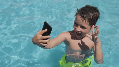 Happy-boy-playing-with-Smartphone-in-Swimming-pool,-Smiling-while-taking-photos-and-Videos