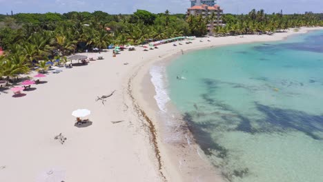 Drone-flight-over-sandy-beach-with-sunshades-in-front-of-luxury-private-Caribbean-Sea-in-summer