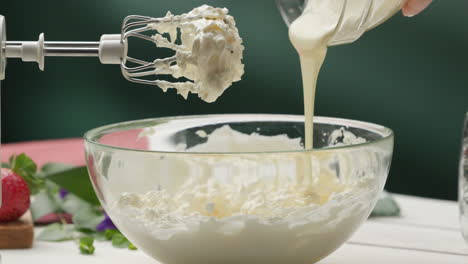 Pouring-melted-white-chocolate-into-glass-bowl-with-whipped-cream
