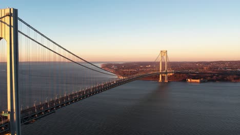 Ascending-aerial-view-in-front-of-the-Verrazzano-Narrows-bridge,-golden-hour-in-New-York,-USA