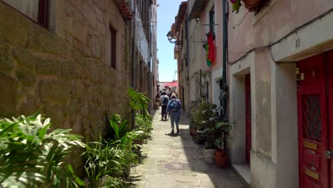 Turistas-Caminando-En-Un-Callejón-Estrecho-Con-Plantas-Y-Coloridos-Balcones-Cerca-De-La-Picota-De-La-Plaza-De-Porto