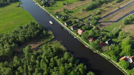 Luftaufnahme-Eines-Bootes,-Das-Auf-Dem-Fluss-Mit-Villen-Am-Wasser-In-Ossenzijl-In-Friesland,-Niederlande,-Segelt
