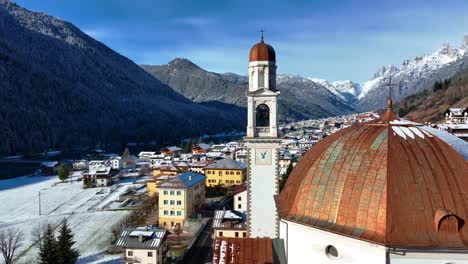 Drone-Aerial-view-of-church-and-bell-tower-of-a-small-town-in-the-mountains-with-snow-in-winter