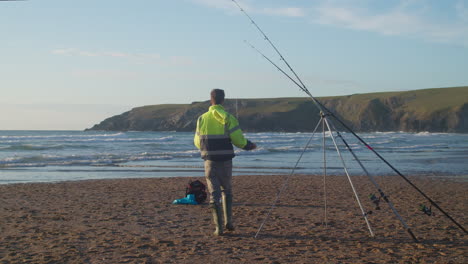 Man-Setting-Up-His-Fishing-Rod-On-The-Shore-In-Holywell-Bay,-Cornwall,-England---wide-shot