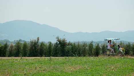 Couple-With-Their-Children-Riding-Four-wheeled-Bicycle-At-Anseong-Farmland-with-Mountains-in-Background
