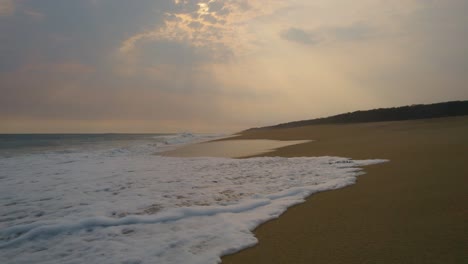 Luftaufnahme,-Die-Bei-Sonnenaufgang-Tief-über-Den-Strand-Von-Oaxaca-Fliegt,-Während-Wellen-über-Die-Sandige-Küste-Mexikos-Spülen