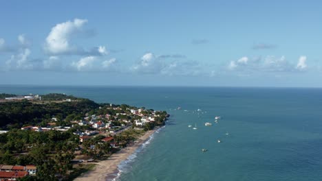 Dollyout-aerial-drone-shot-of-the-beautiful-tropical-Seixas-beach-coastline-near-the-capital-city-of-Joao-Pessoa-in-Paraiba,-Brazil-with-small-boats-docked-next-to-the-small-town-full-of-tourists