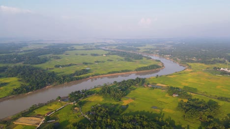 Discover-the-beauty-of-Bangladesh's-rural-landscape-in-this-stunning-aerial-footage,-showcasing-the-vast-and-vibrant-farmland,-peaceful-river,-quaint-countryside-villages,-and-lush-greenery